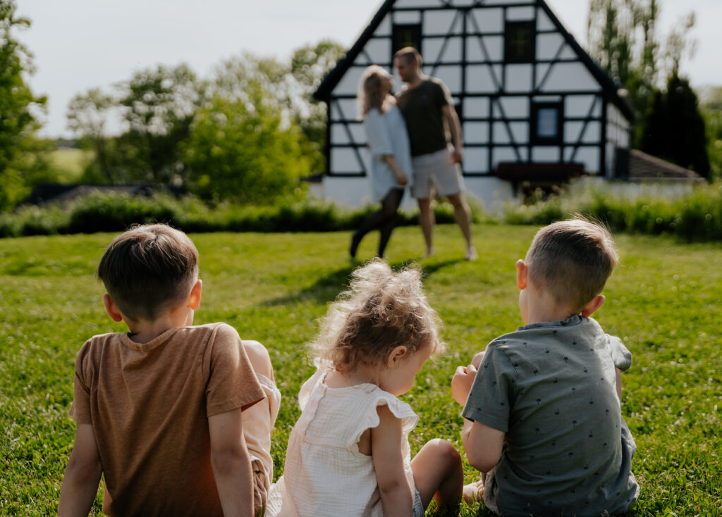 3 Kinder sitzen mit dem Rücken zur Kamera und beobachten ihre Eltern.